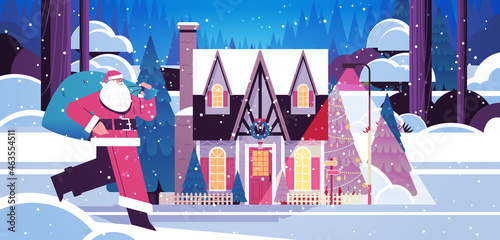 santa claus running with sack full of gifts near snow covered decorated house new year and christmas holidays celebration
