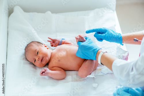 Unrecognizable pediatrician hands in blue gloves check feet of newborn baby in hospital. photo