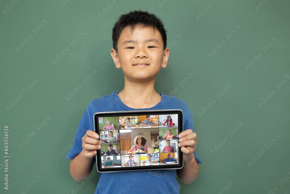 © vectorfusionart - Smiling asian boy holding tablet for video call, with diverse elementary school pupils on screen © vectorfusionart - Smiling asian boy holding tablet for video call, with diverse elementary school pupils on screen