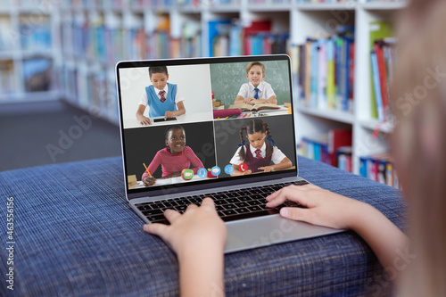 Caucasian girl using laptop for video call, with smiling diverse elementary school pupils on screen