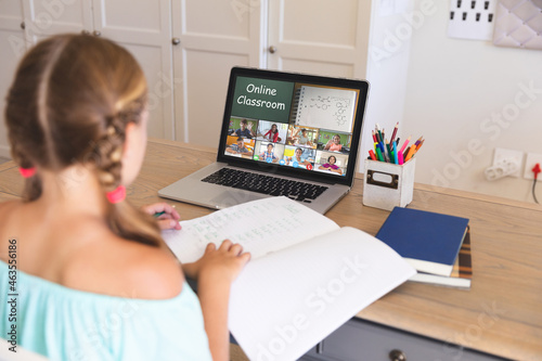 Caucasian girl using laptop for video call, with diverse elementary school pupils on screen
