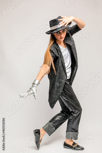 Konstfotografi A young pretty teenage girl in a man's black suit and hat dances in the studio o