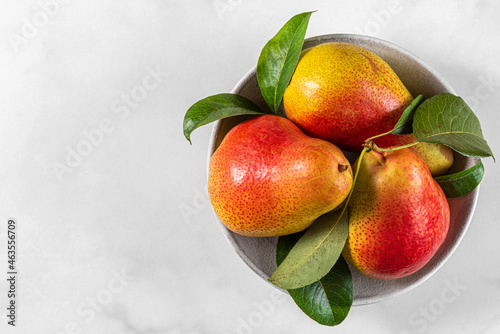 Fresh ripe pears with green leaves in a bowl on white background. Top view with copy space