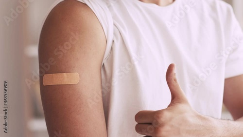 Flu shot. Coronavirus vaccine. Effective immunization. Unrecognizable satisfied male patient showing patch on arm shoulder after getting covid-19 jab recommending with thumb up. photo