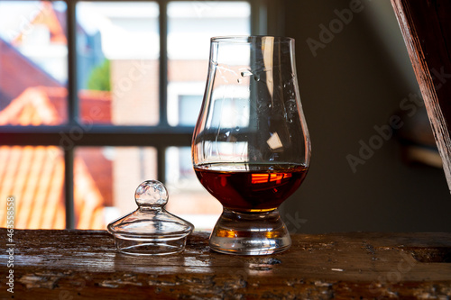 Dram of single malt scotch whisky served in tasting glass with view on old window and houses