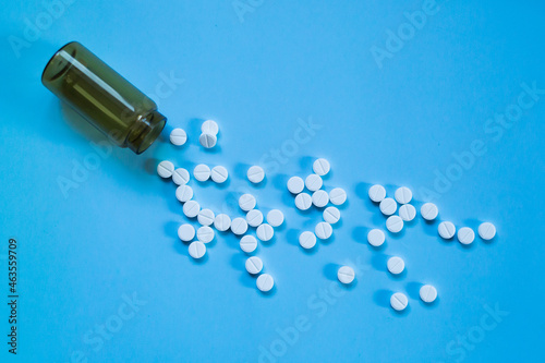 White medical pills and tablets spilling out of a drug bottle on a blue background.