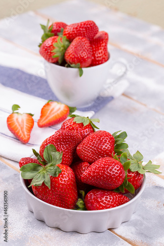 Juicy strawberries in a white ceramic bowl and cup on a gray shabby wooden table in a rustic style  copy space  vertical photo