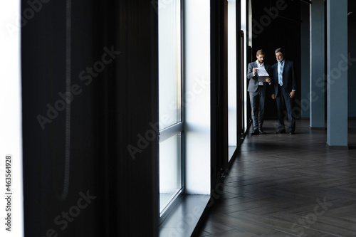 Two colleagues communicating in corridor, partners walking in the modern office