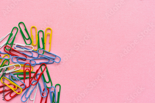 Office paper clips isolated on pink background. Pink, red, blue, green, orange colorful Plastic paper clips for office supplies documents. Flat lay, top view.