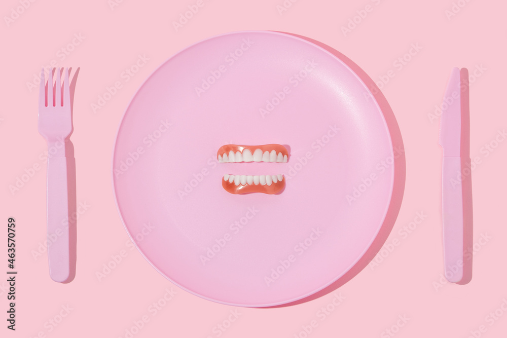 Creative layout with pastel pink plate, fork,knife and false or fake teeth on pastel pink background.Minimal surreal breakfast idea or food restaurant concept. 80s 90 aesthetic fashion dentist idea. Creative layout with pastel pink plate, fork,knife and false or fake teeth on pastel pink background.Minimal surreal breakfast idea or food restaurant concept. 80s 90 aesthetic fashion dentist idea.