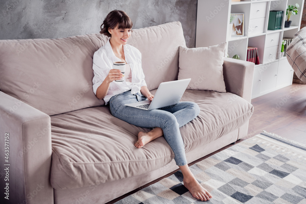 Photo portrait woman wearing white shirt using computer browsing internet drinking coffee at home on couch Photo portrait woman wearing white shirt using computer browsing internet drinking coffee at home on couch