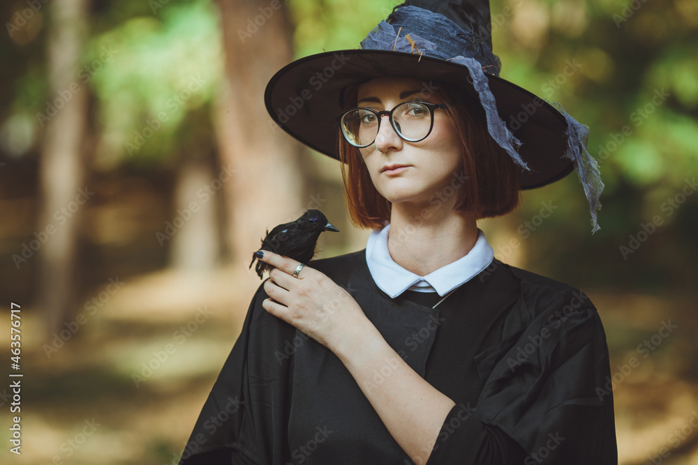Halloween witch. Portrait of a girl in a hat and witch costume and with a black raven in the forest. Ready for the holiday wallet or life