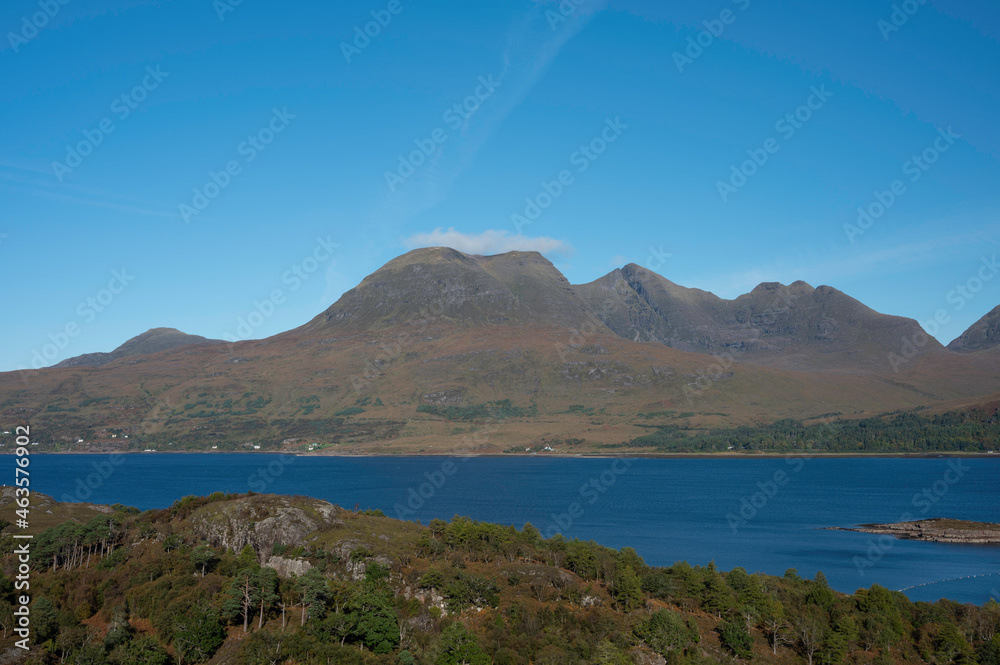 View over forest and Loch Torridon to Beinn Alligin mountain in the Scottish Highlands. Sunny day with blue. Clear view of ridgeline and horns of Alligin. No people.