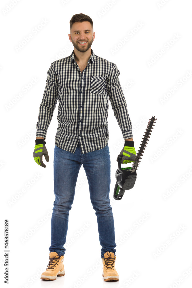Smiling young man is standing with electric saw. Front view. Full length isolated on white. Smiling young man is standing with electric saw. Front view. Full length isolated on white.