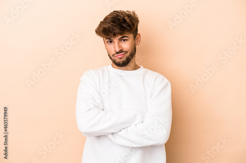 Young arab man isolated on beige background suspicious, uncertain, examining you.