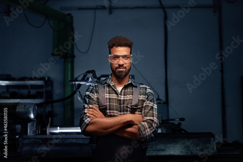 Portrait of young industrial man working indoors in metal workshop, looking at camera.
