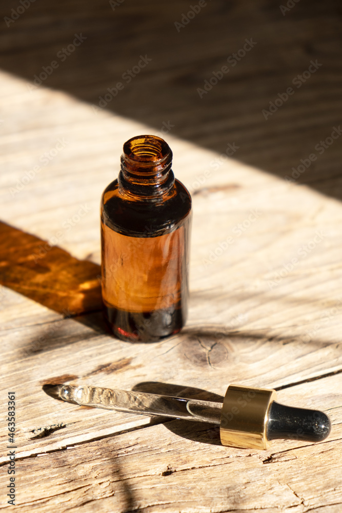 Dark amber glass bottle with dropper for oil, lotion or serum on a aged wooden background with a hard shadow of tropical palm leaves. Presentation of a cosmetic product. Layout of the beauty salon . Dark amber glass bottle with dropper for oil, lotion or serum on a aged wooden background with a hard shadow of tropical palm leaves. Presentation of a cosmetic product. Layout of the beauty salon .