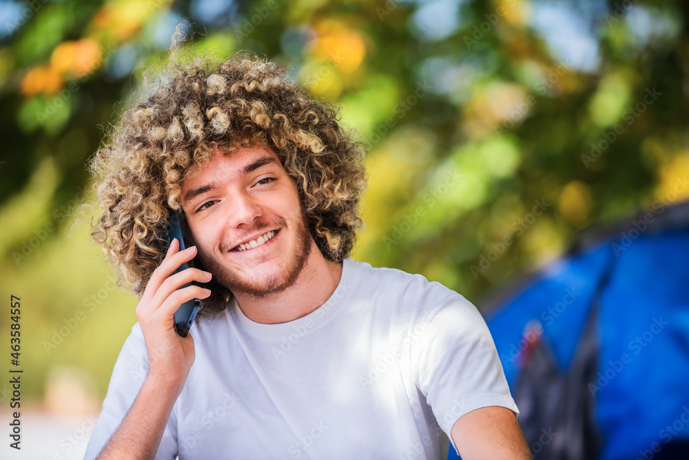 A smiling Afro man sitting in nature and talking on a smartphone A smiling Afro man sitting in nature and talking on a smartphone