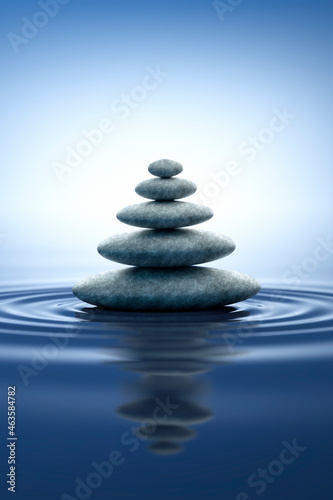 Stack of stones with ripples in the water with blue reflections - zen and nature concept
