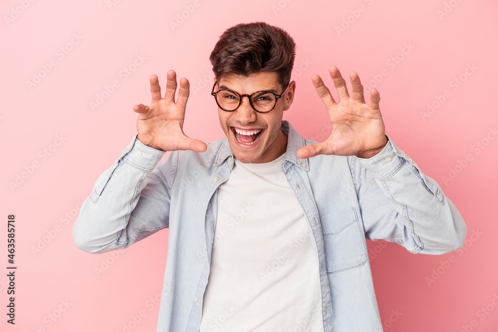 Young caucasian man isolated on pink background showing claws imitating a cat, aggressive gesture. Young caucasian man isolated on pink background showing claws imitating a cat, aggressive gesture.