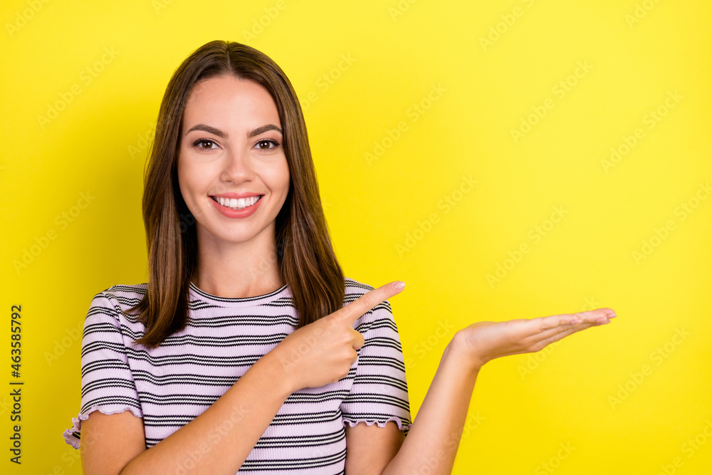 Photo of cute millennial brunette lady point hold empty space wear striped t-shirt isolated on yellow background Photo of cute millennial brunette lady point hold empty space wear striped t-shirt isolated on yellow background