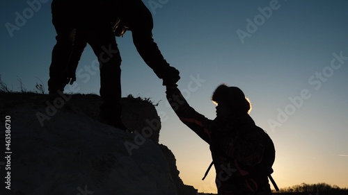 Travelers help each other to climb cliff. Silhouettes of climbers reach out to each other, climbing to the top of the mountain. Teamwork of business people. A team of businessman goes to success wins.