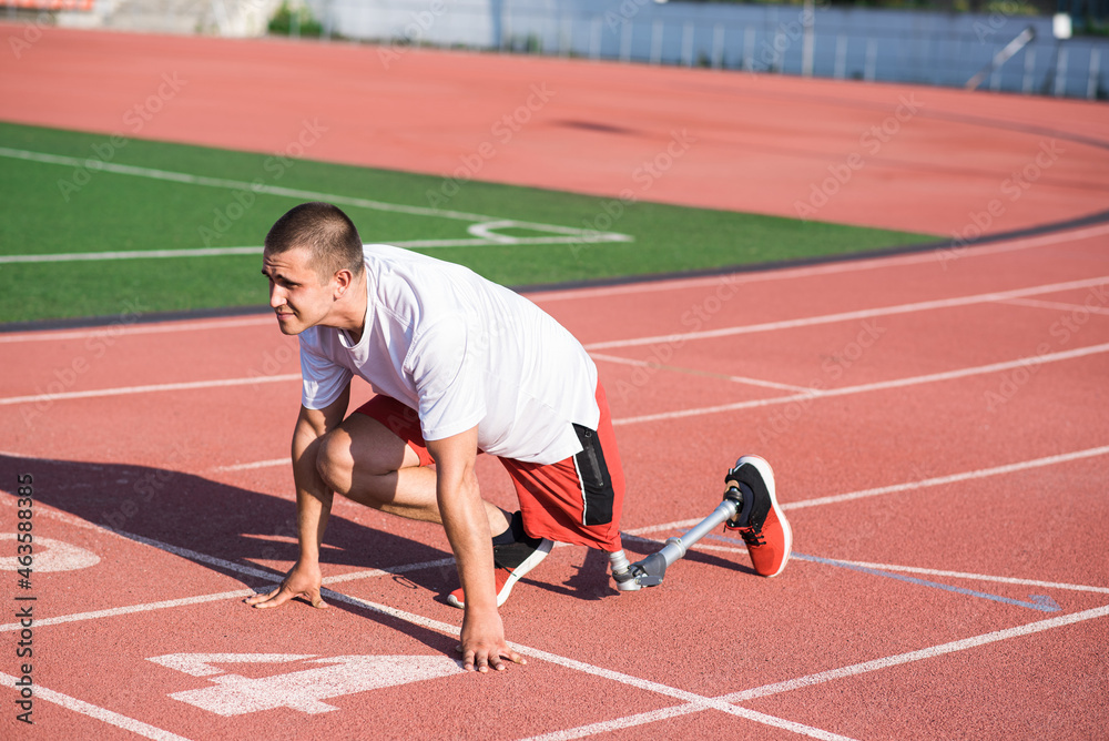 Obraz premium Caucasian male athlete with a prosthetic leg standing at the start on the track at the stadium. Sport concept.