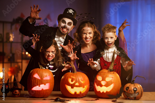 Young caucasian family mother father and children in Halloween costumes and makeup making scary gesture, saying trick or treat while celebrating together all hallows eve in dark room at home