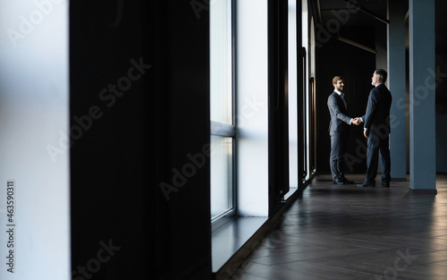 Full length view of businessmen shaking hands in office building.