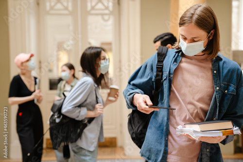 Young european students in face mask standing at library hallway