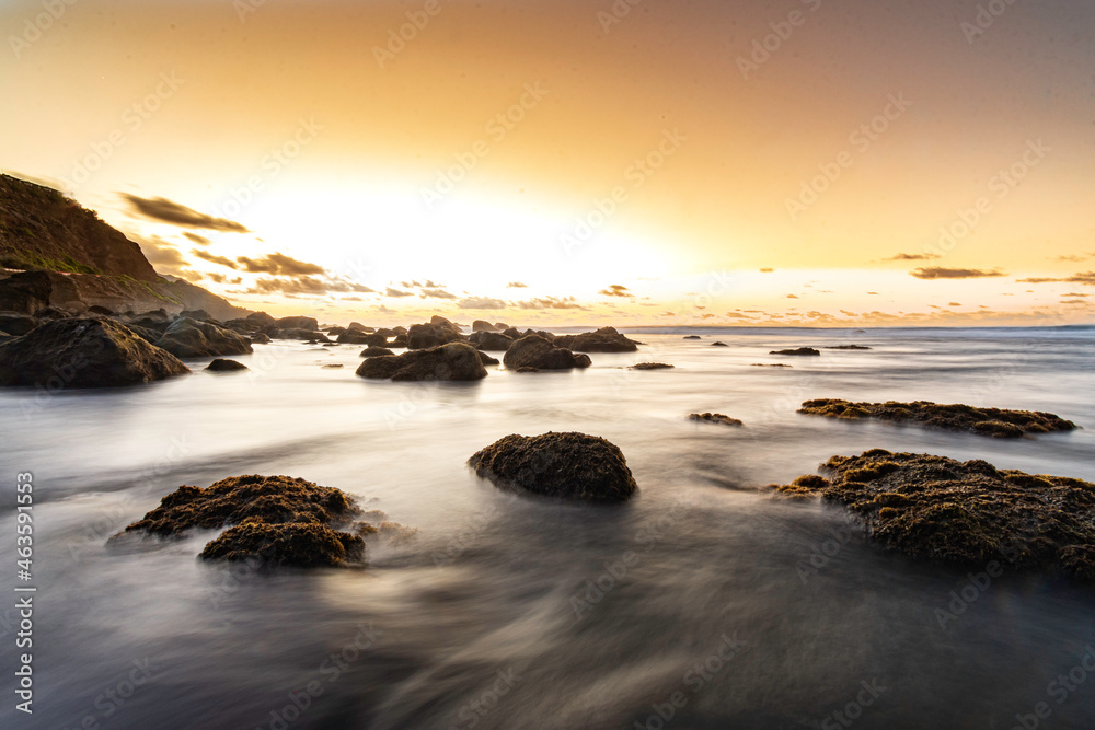 sunset at Almaciga beach with rocks in the foreground.
