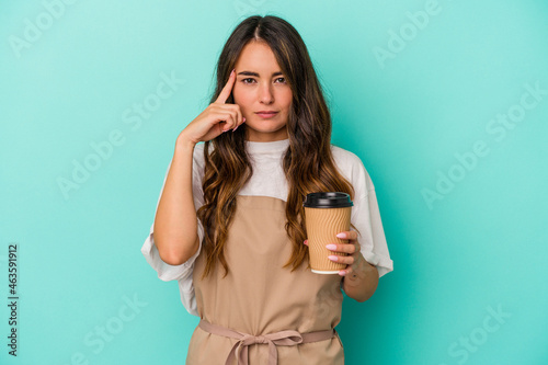 Young caucasian store clerk woman holding a takeaway coffee isolated on blue background pointing temple with finger, thinking, focused on a task.