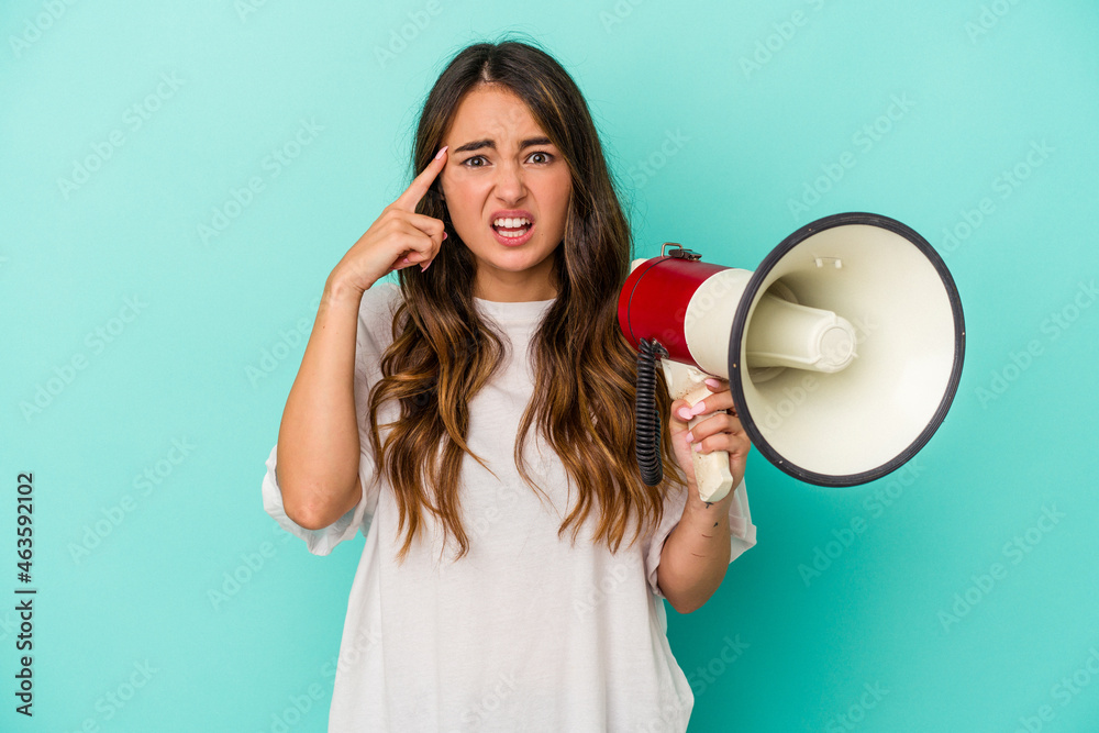 Young caucasian woman holding a megaphone isolated on blue background showing a disappointment gesture with forefinger. Young caucasian woman holding a megaphone isolated on blue background showing a disappointment gesture with forefinger.