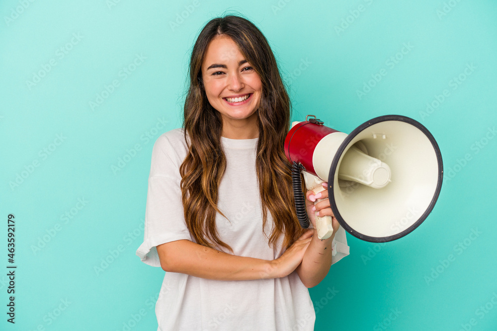 Young caucasian woman holding a megaphone isolated on blue background laughing and having fun. Young caucasian woman holding a megaphone isolated on blue background laughing and having fun.