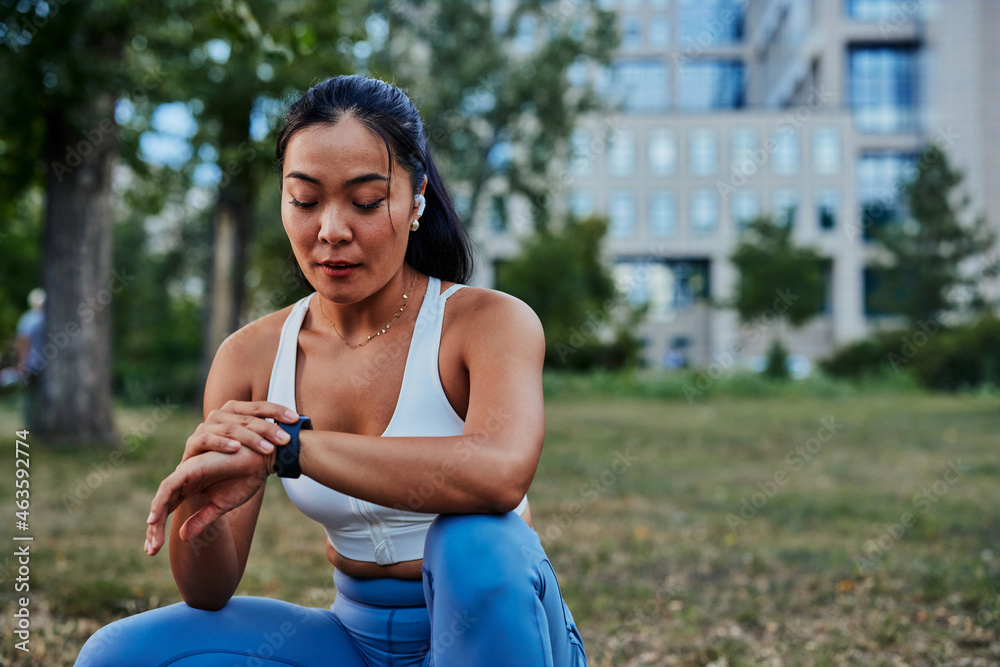 Beautiful sportswoman setting up smart watch during workout in park Beautiful sportswoman setting up smart watch during workout in park