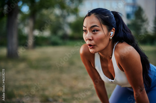 Asian woman taking a moment to catch her breath after workout in park photo