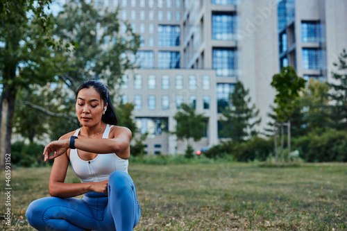 Young sportswoman looking and touching on smartwatch screen while exercise outdoors © bernardbodo