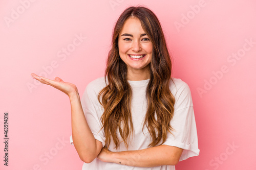 Young caucasian woman isolated on pink background showing a copy space on a palm and holding another hand on waist.