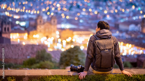 Asian man traveler and photograpaher sitting on viewpoint looking at illuminated cusco city at night. Cusco (Cuzco) is a city in southeastern Peru, near the Urubamba Valley of the Andes mountain range photo