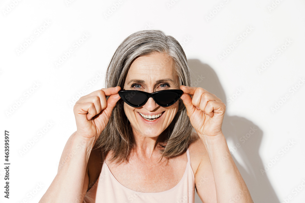 Naklejka premium Mature woman holding sunglasses while laughing at camera