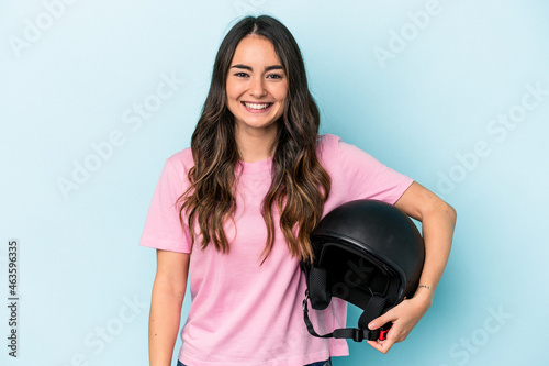 Young caucasian woman holding a motor bike helmet isolated on blue background happy, smiling and cheerful.