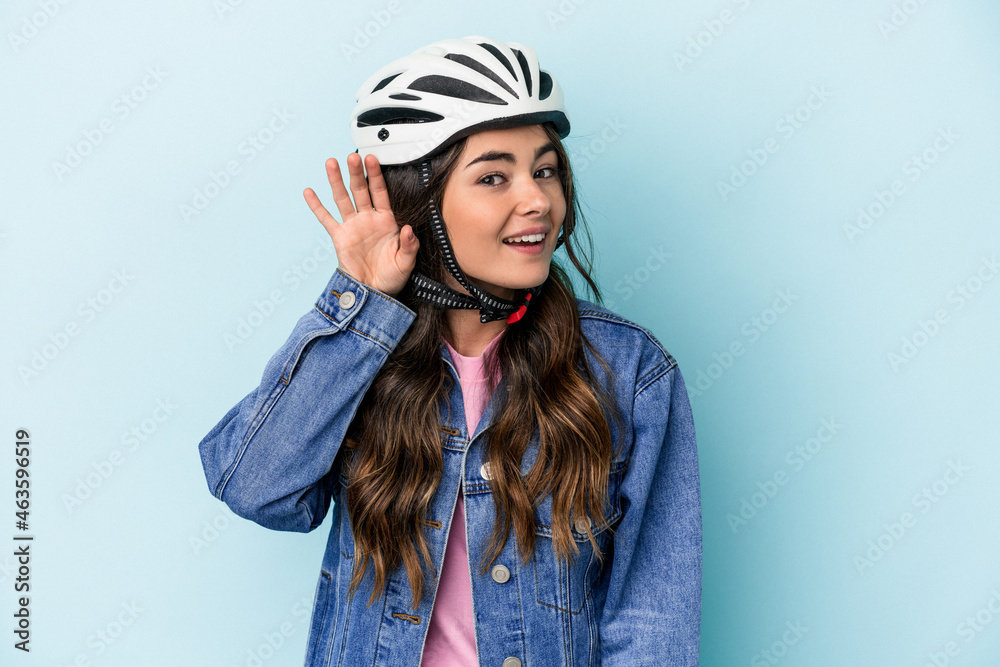 Young caucasian woman rinding a bike isolated on blue background trying to listening a gossip. Young caucasian woman rinding a bike isolated on blue background trying to listening a gossip.