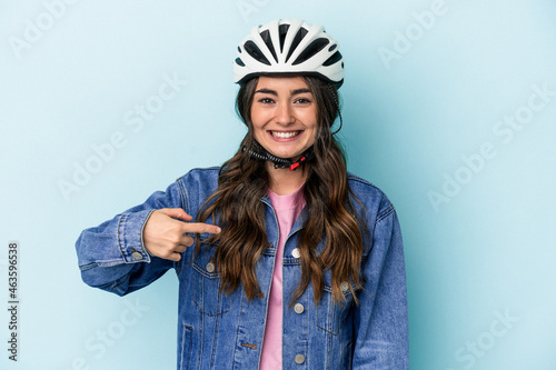 Young caucasian woman rinding a bike isolated on blue background person pointing by hand to a shirt copy space, proud and confident © Asier