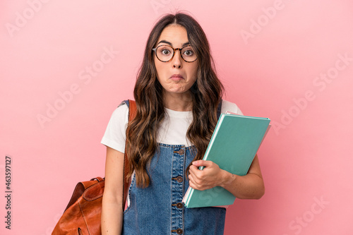 Young caucasian student woman isolated on pink background shrugs shoulders and open eyes confused.