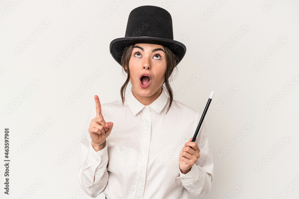 Young magician woman holding a wand isolated on white background pointing upside with opened mouth.