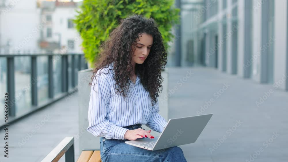 Good looking caucasian woman having free time while sitting on the bench with a laptop at her knees. Outdoors Good looking caucasian woman having free time while sitting on the bench with a laptop at her knees. Outdoors