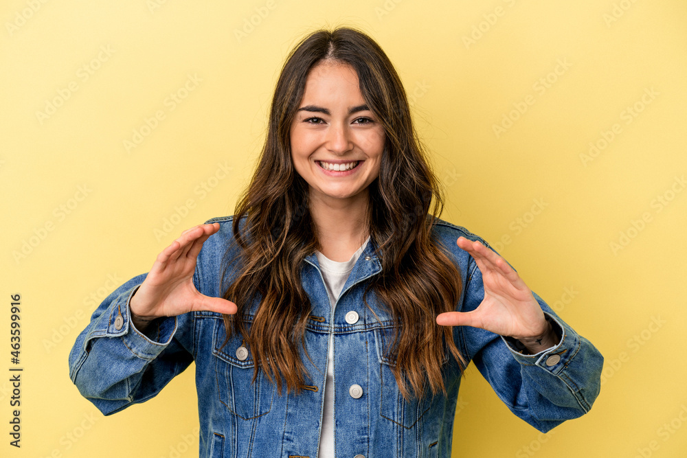 Young caucasian woman isolated on yellow background holding something with palms, offering to camera. Young caucasian woman isolated on yellow background holding something with palms, offering to camera.