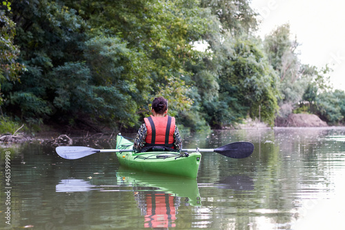 Young woman in green kayak paddle at river near trees