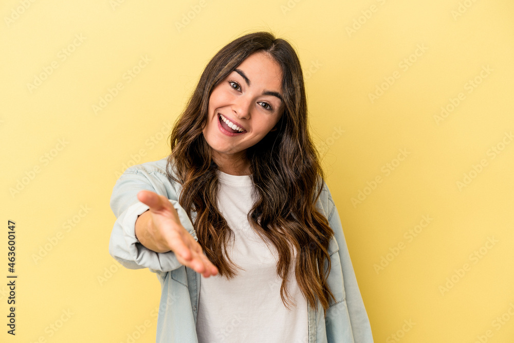 Young caucasian woman isolated on yellow background stretching hand at camera in greeting gesture. Young caucasian woman isolated on yellow background stretching hand at camera in greeting gesture.