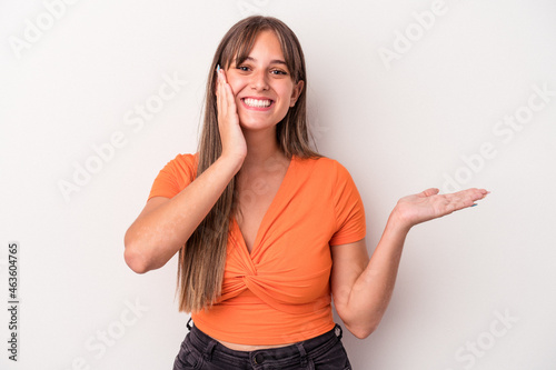 Young caucasian woman isolated on white background holds copy space on a palm, keep hand over cheek. Amazed and delighted.